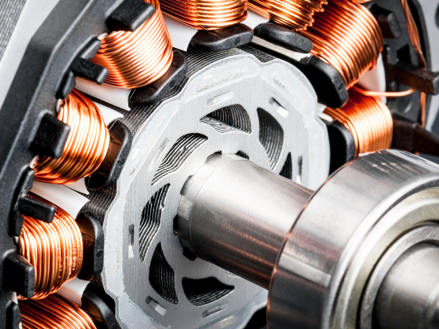 Close-up of an electric motor showing copper windings, laminated steel stator, rotating shaft and bearing.
