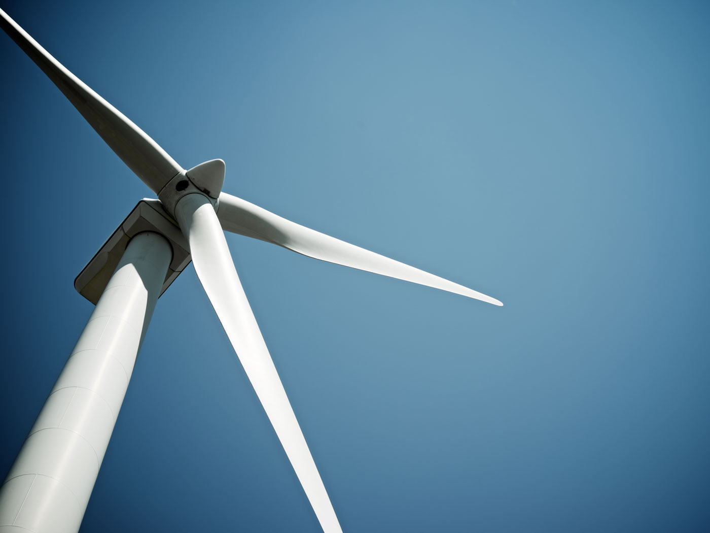 Low-angle view of a white three‑blade wind turbine against a clear blue sky, highlighting clean renewable energy.